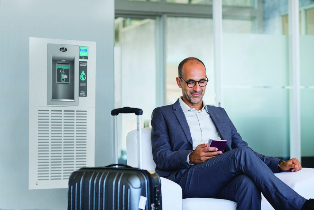 Business traveler seated near an Oasis Coolers hydration station, ensuring convenient access to clean drinking water in transit hubs